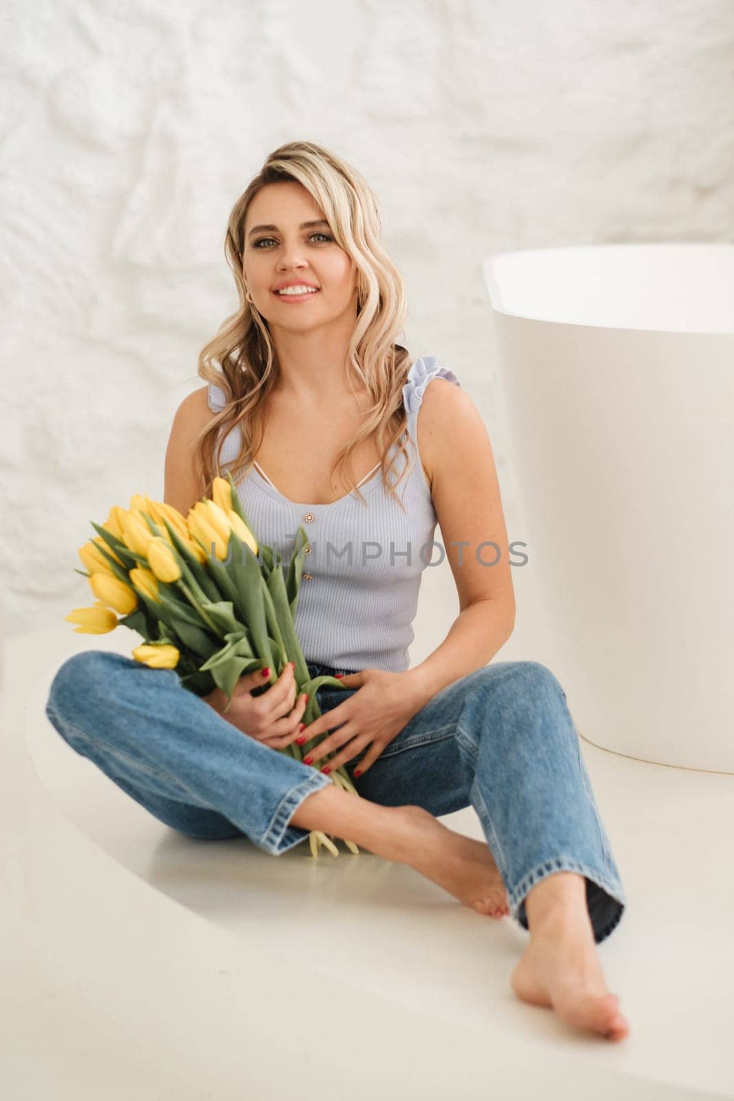 Cute smiling girl with a bouquet of yellow tulips in the interior by Lobachad