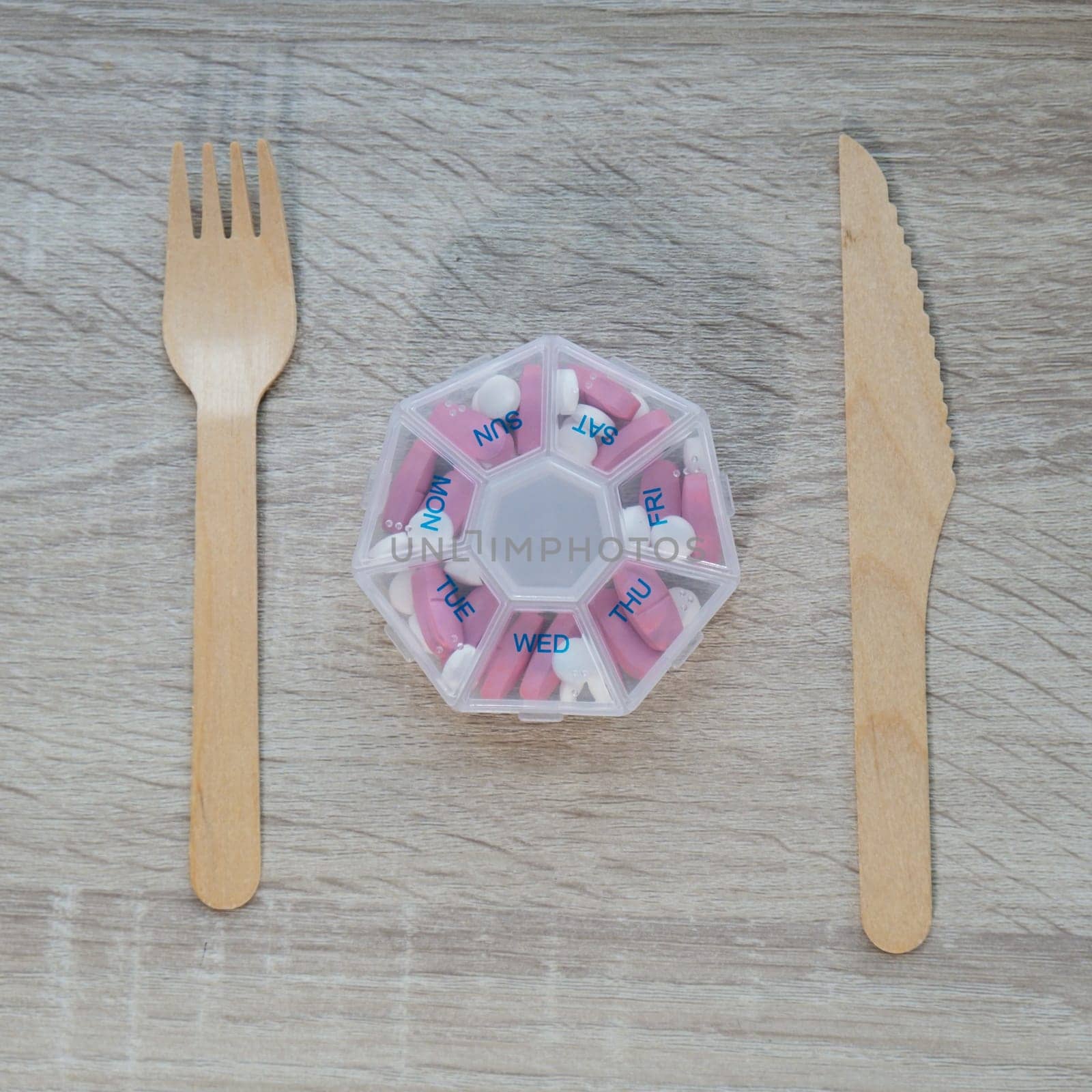 Organizer weekly shots with fork and knife medical pill box with doses of tablets for daily take medicine with white pink drugs and capsules. Daily vitamins at home. Health care and diseases cure by anna_stasiia