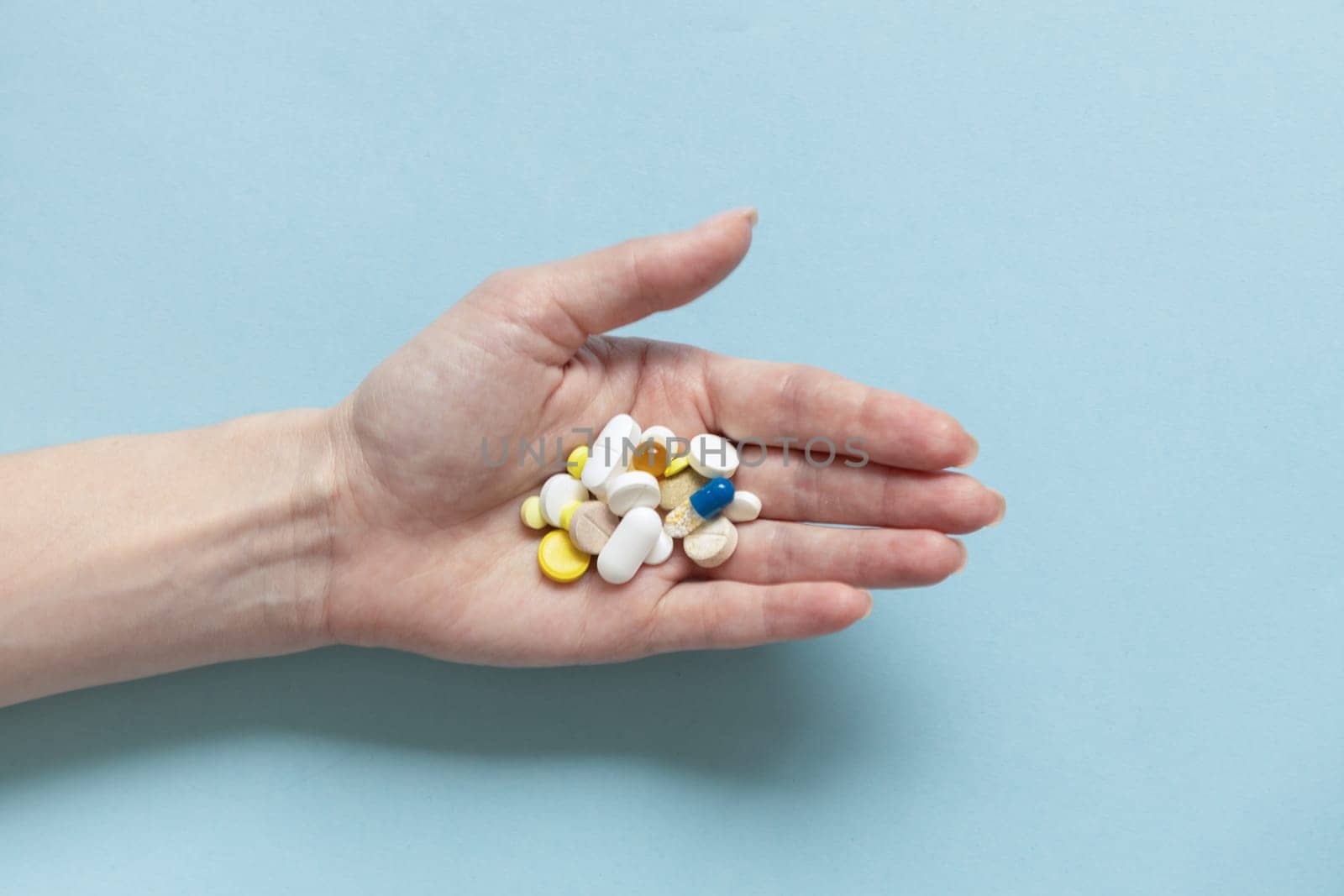 Pills in woman hand on pastel blue background
