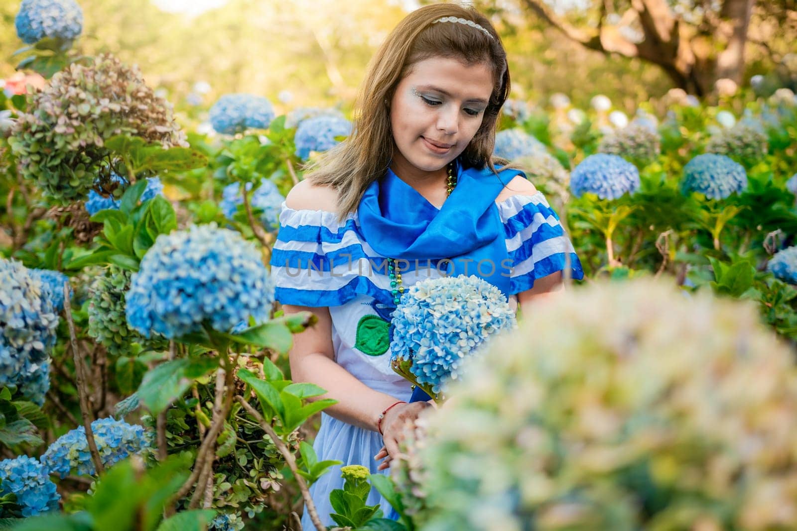 Portrait of girl in traditional Central American folk costume holding flowers in a nursery. Beautiful Nicaraguan woman in national folk costume holding flowers in a nursery by isaiphoto