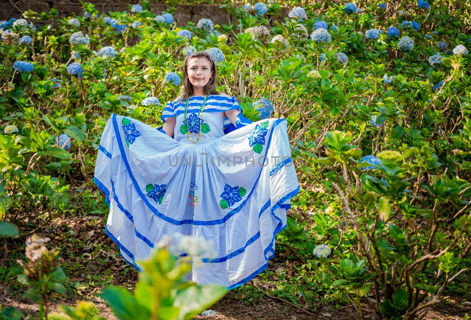 Young Nicaraguan woman in traditional folk costume in a field of Milflores, Smiling woman in national folk costume in a field surrounded by flowers. Nicaraguan national folk costume