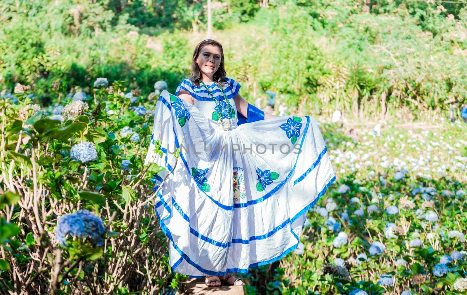 Smiling woman in national folk costume in a field surrounded by flowers. People in Nicaraguan national folk costume. Young Nicaraguan woman in traditional folk costume in a field of Milflores by isaiphoto