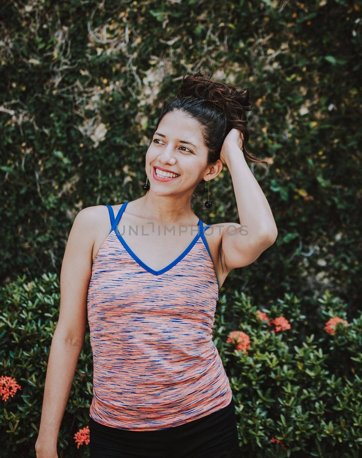 Smiling latin woman near a garden with defocused background, Portrait of smiling woman near a grass wall. Close-up of happy girl near a garden outdoors by isaiphoto