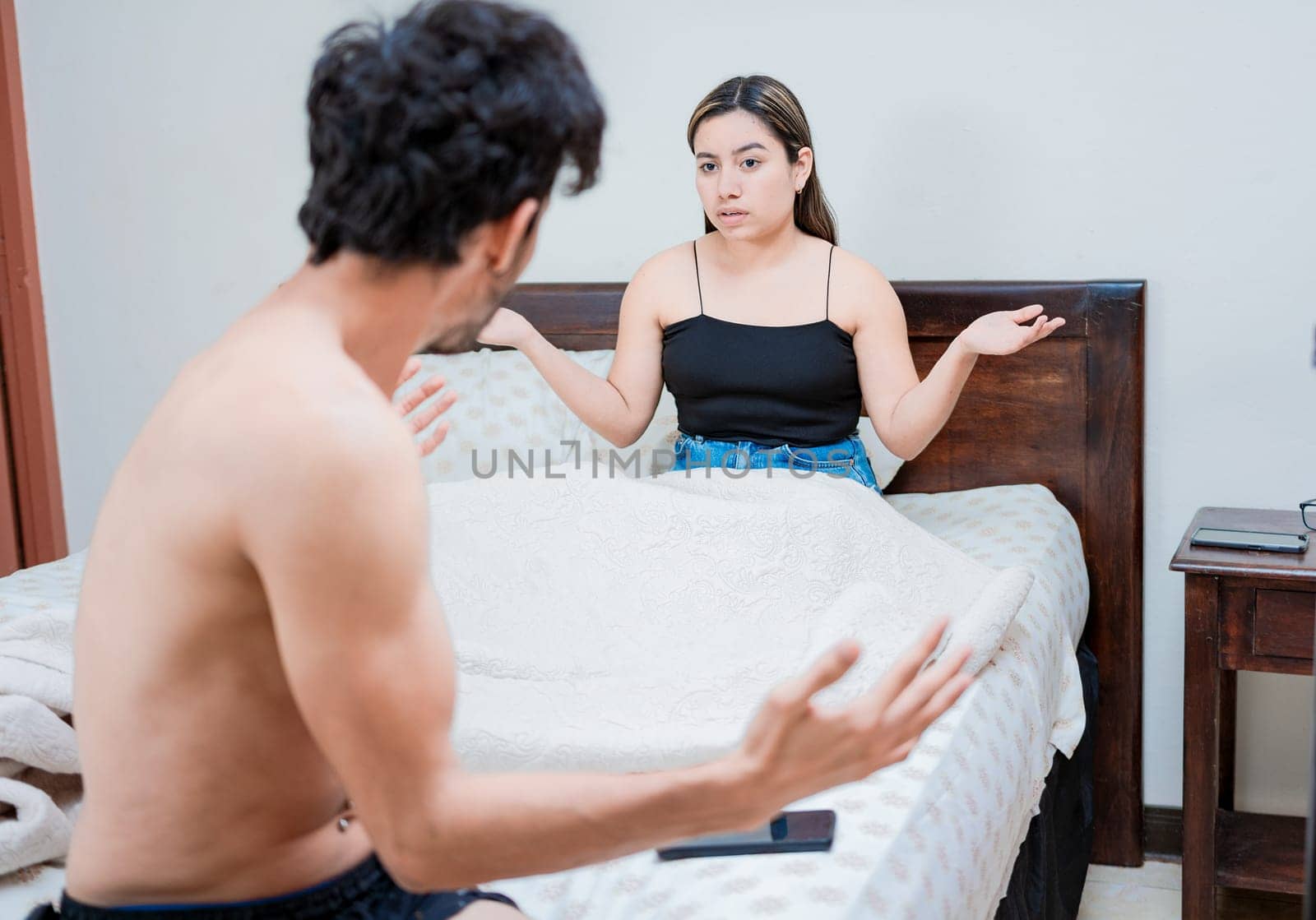 Upset wife with husband in bedroom bed, Young couple arguing in bed room. Concept of couple problems in bed, Husband fighting with his wife in bed by isaiphoto