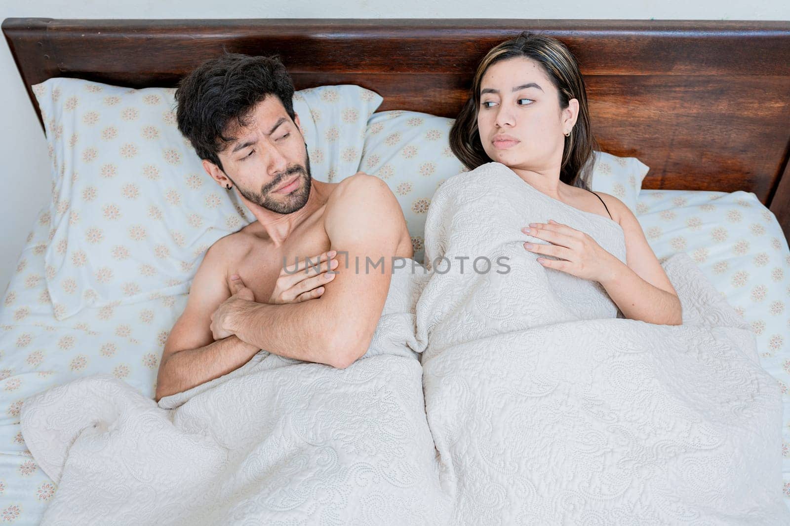 Upset couple in bed with crossed arms. Woman lying in bed upset with her husband. Angry man and woman in bed with crossed arms. Marriage problems concept by isaiphoto