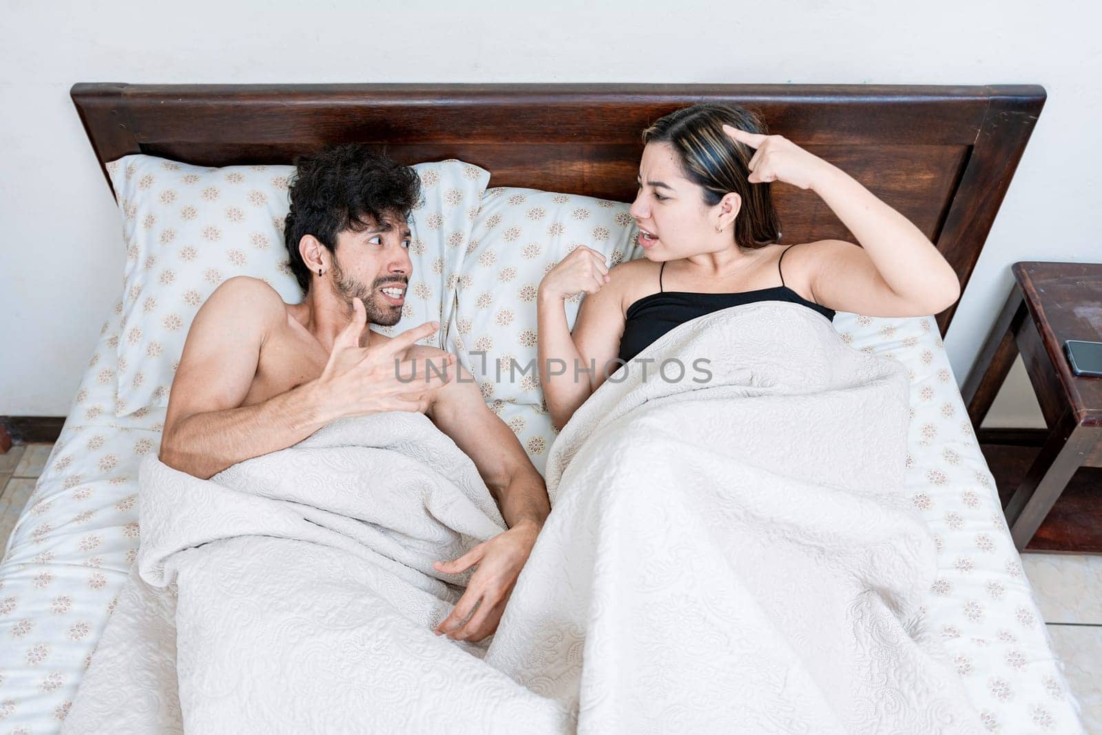 Upset couple lying in bed arguing. Top view of young couple lying in bed arguing. Upset couple lying in bed arguing. Marriage problems concept