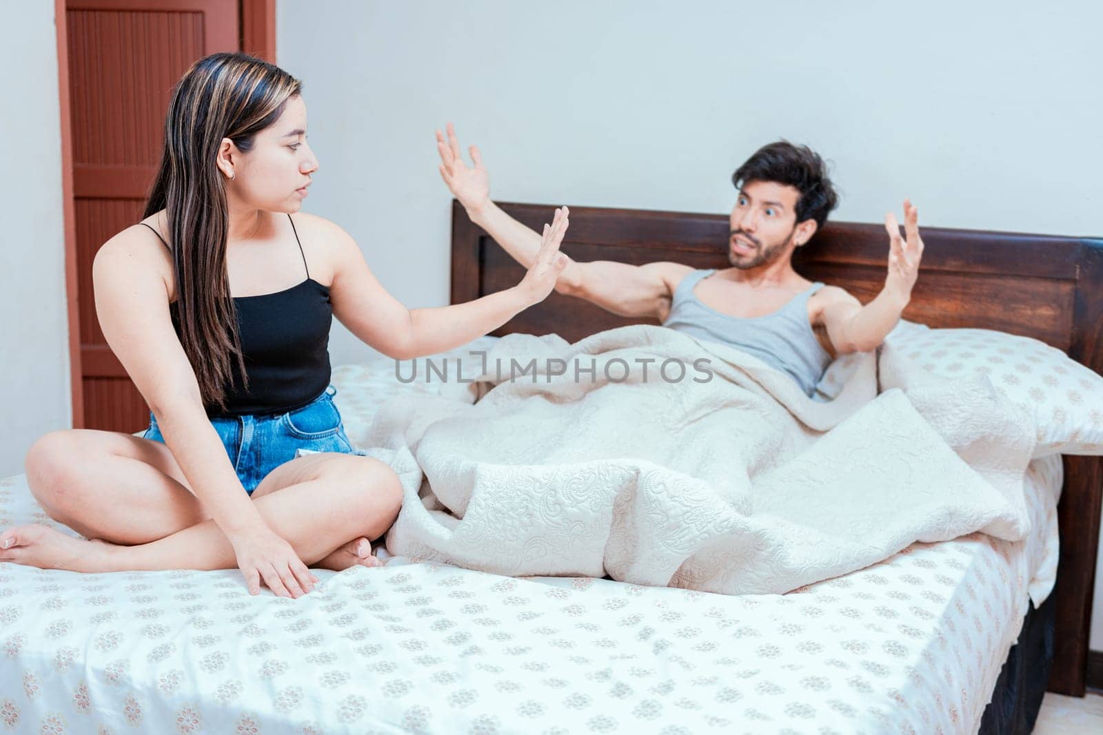 Upset woman with husband in bedroom bed, Husband fighting with his wife in bed.  Young couple arguing in bed room. Concept of couple problems in bed by isaiphoto