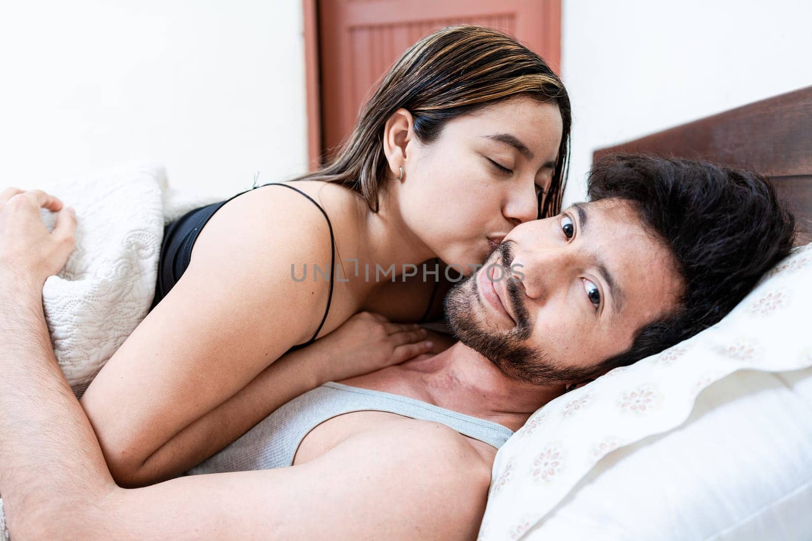 Woman in bed kissing her husband on the forehead. Wife in bed kissing husband on the forehead