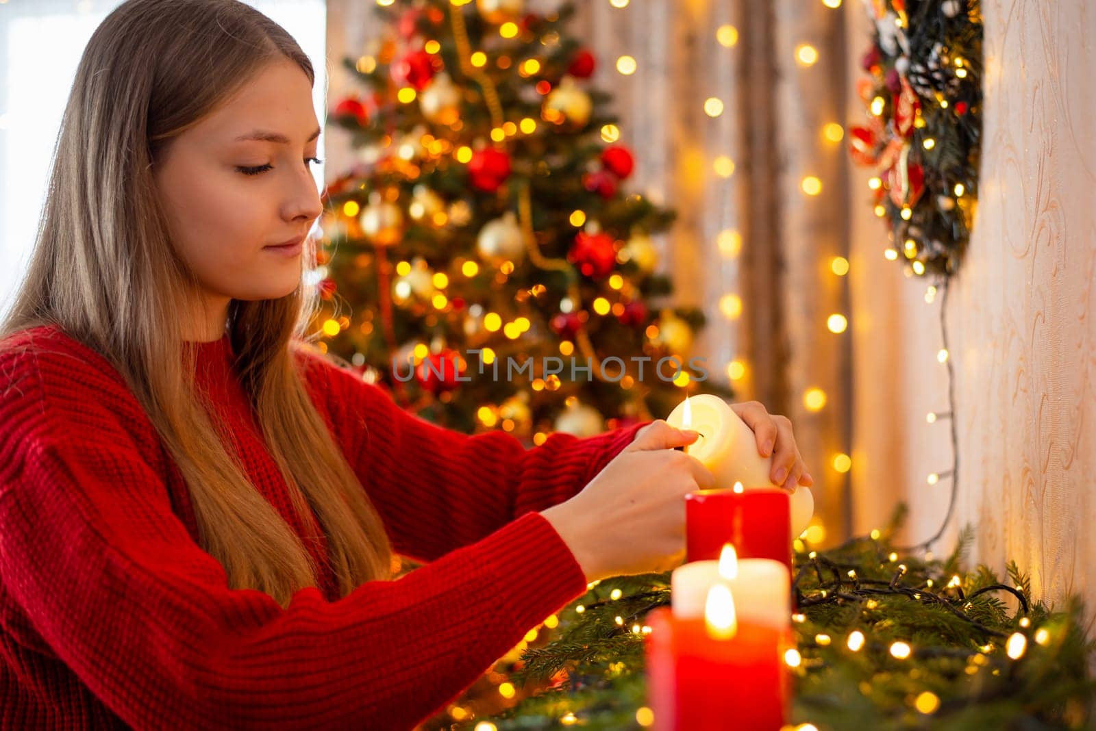 Young blond girl in red sweater igniting candles in decorated living room