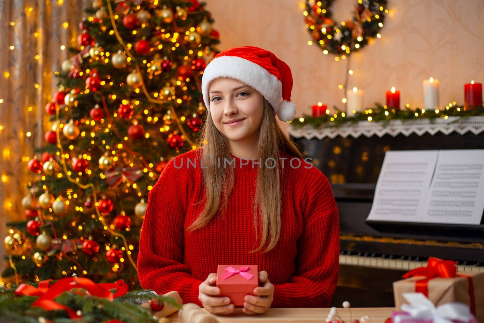 Portrait of a young girl in Santa hat wrapping presents for Christmas for friends and relatives looking to the camera