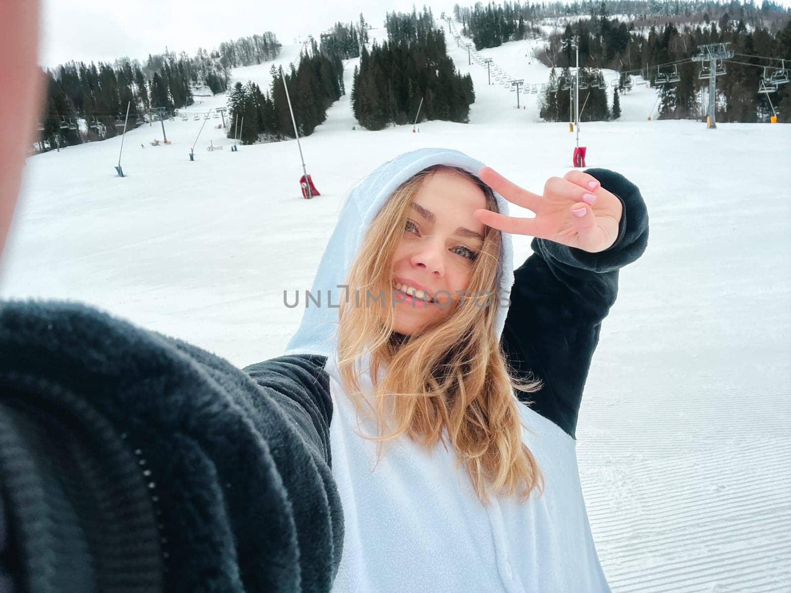 Happy young woman skier taking selfie hiking mountains. Girl smiling Makes Selfie In Ski Clothing On Snow Mountain. Resting relaxing extreme recreation active lifestyle activity technology smart phone mobility internet online concept. Emotions nature on background.