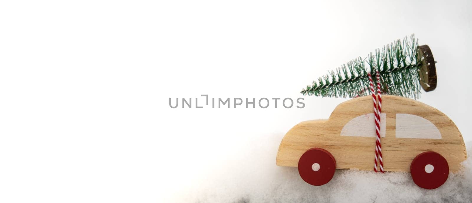 Wooden car carrying Christmas tree over snow. Copy space for text Toy car in snowy landscape. Merry Christmas and Happy New Year concept. Winter is coming Greeting card