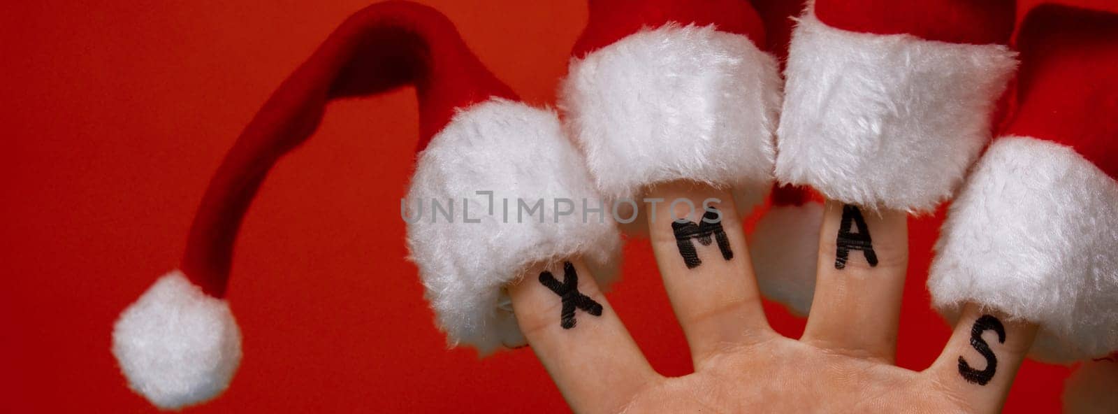 Fingers dressed in Santa-Claus red-white hats and word text XMAS on red background. Concept of Christmas or New Year holidays. Finger family hand