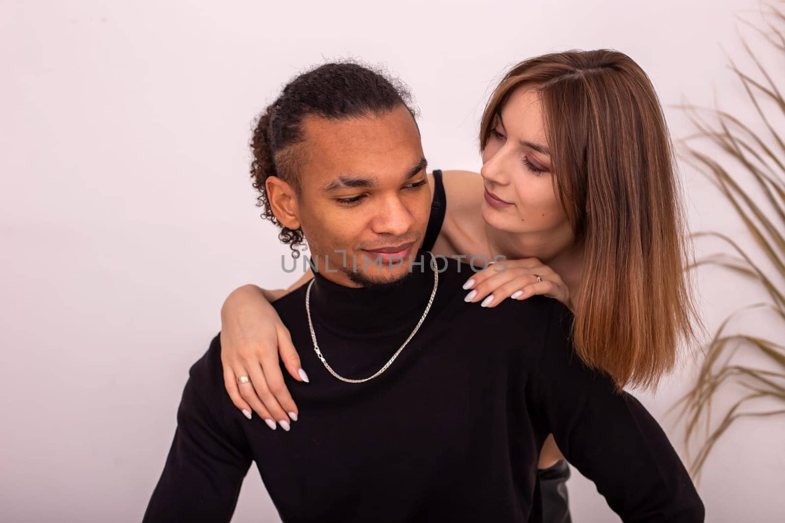 Portrait of beautiful , multiracial couple, in black clothes, near the wall in the room. by Zakharova