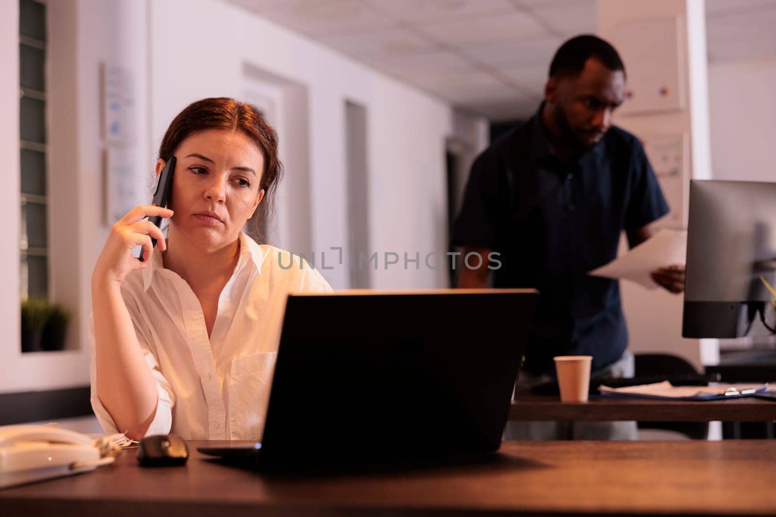 Secretary talking with colleague on smartphone in office by DCStudio