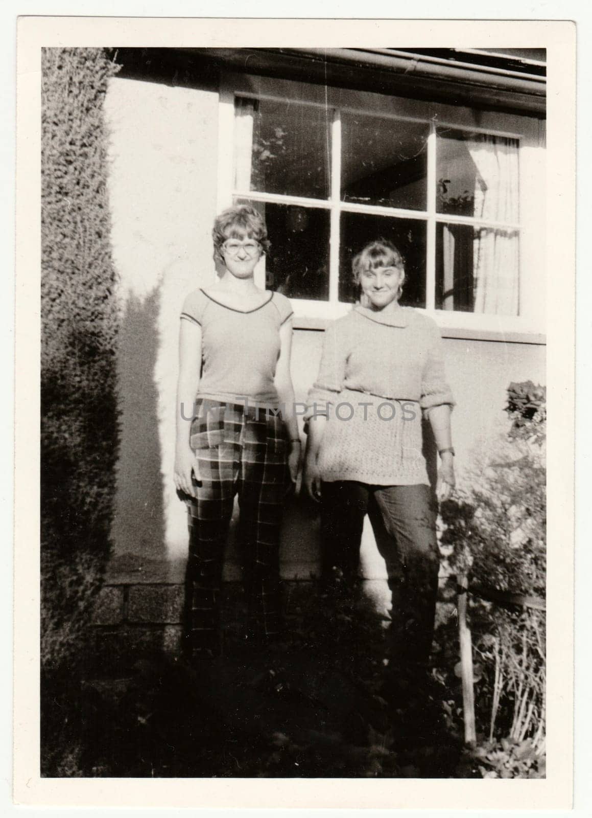 Vintage photo shows young girls in front of country house. Retro black and white photography. by roman_nerud