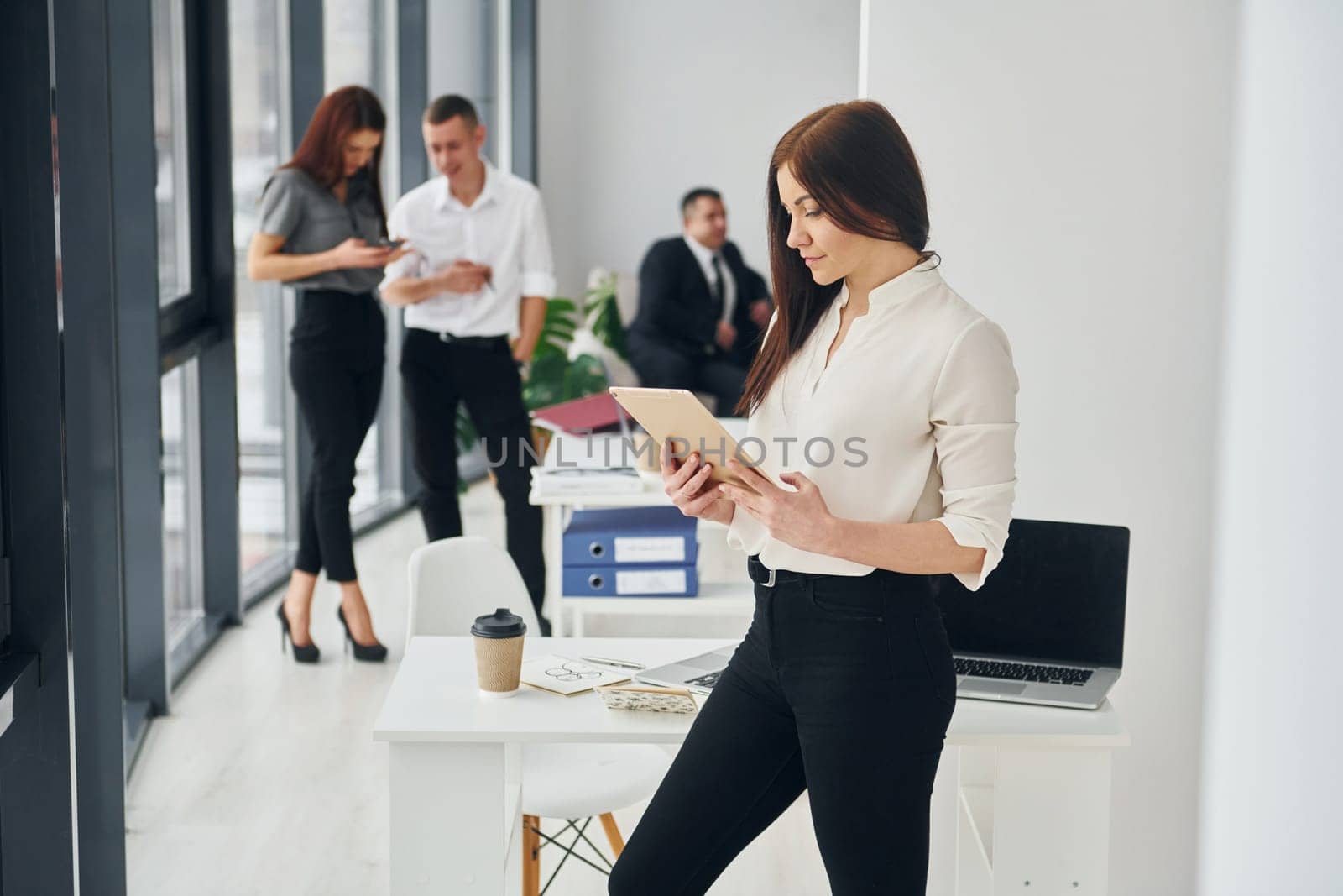 Woman holds tablet. Group of people in official formal clothes that is indoors in the office.