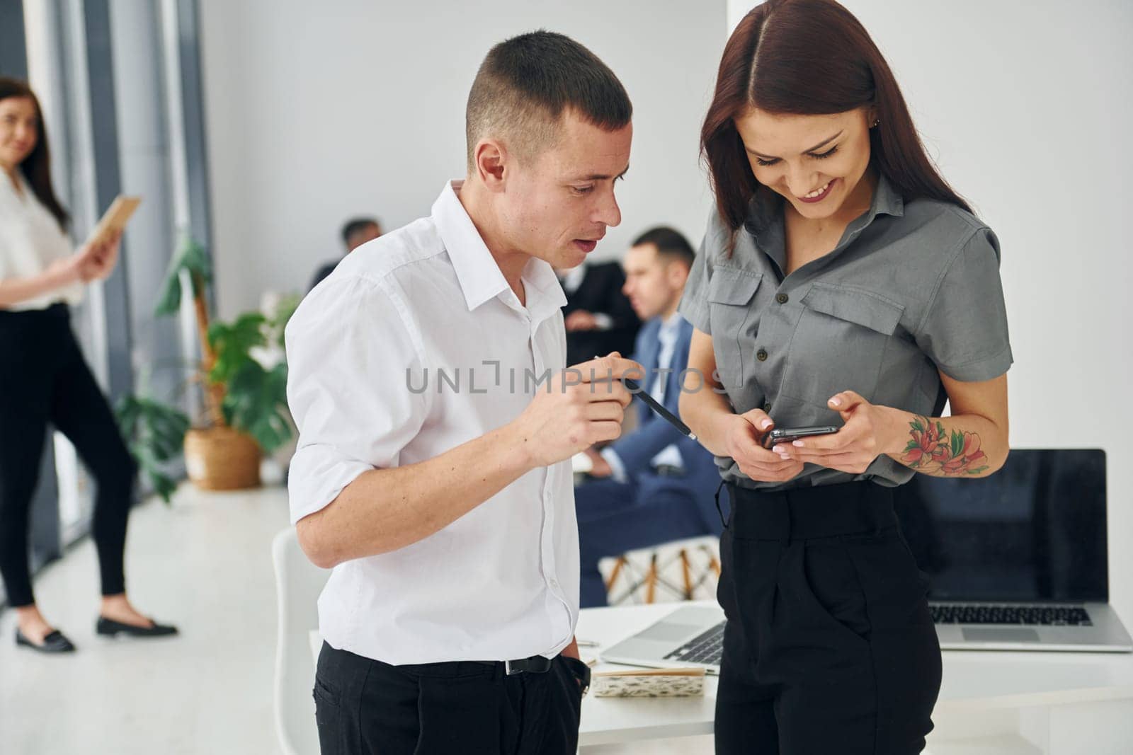 Man with woman using phone. Group of people in official formal clothes that is indoors in the office.