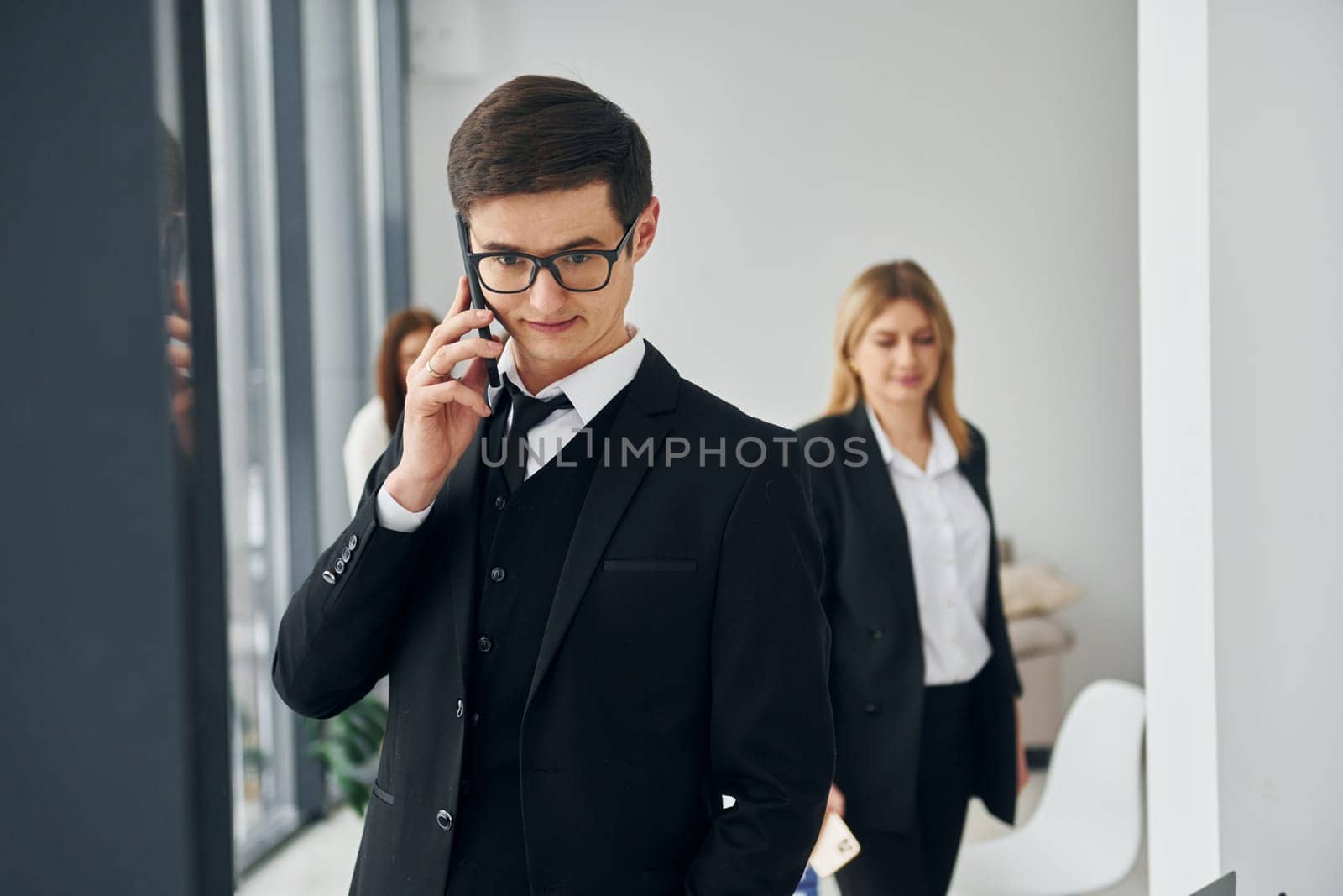 Man talks by phone. Group of people in official formal clothes that is indoors in the office by Standret