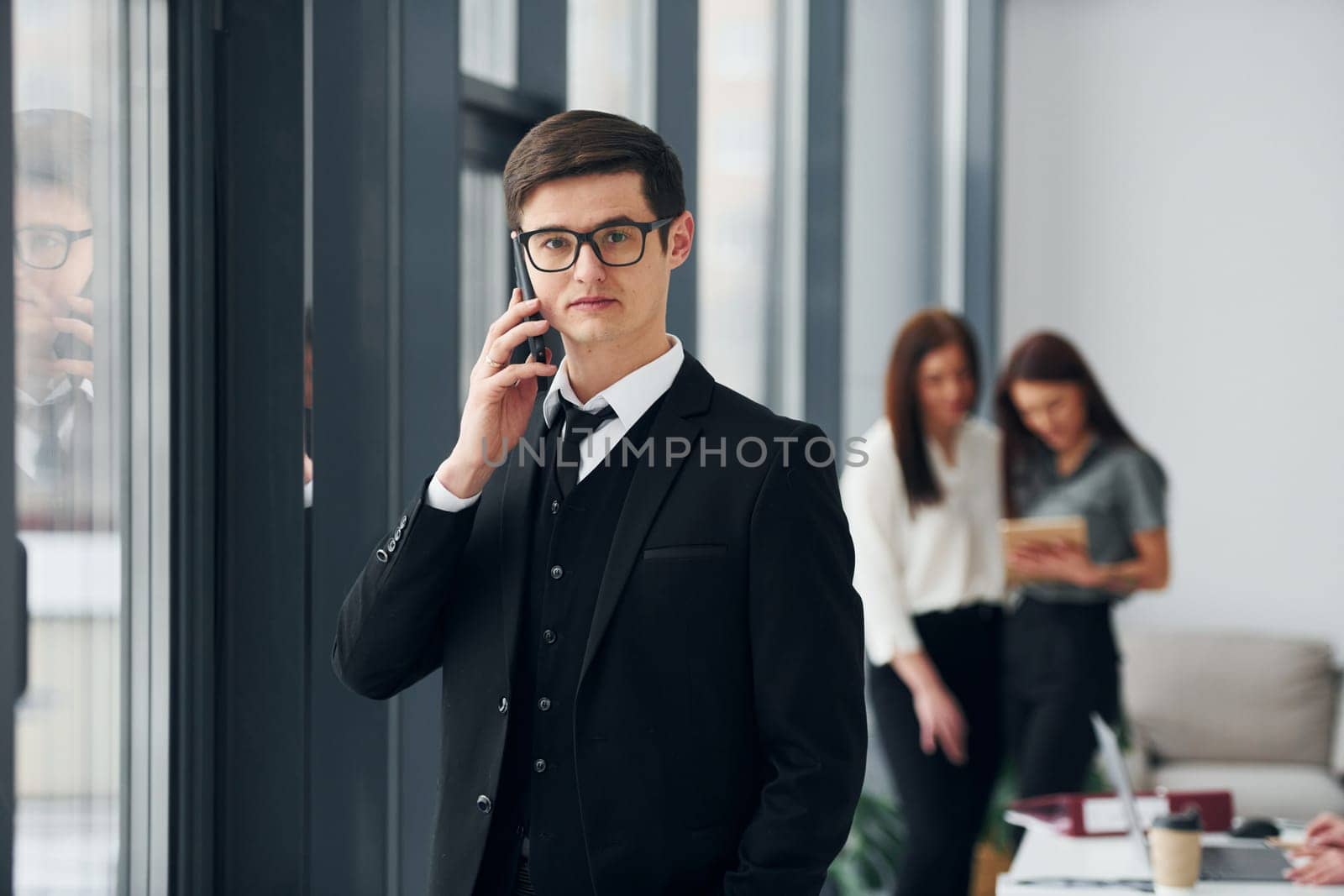 Young man with phone. Group of people in official formal clothes that is indoors in the office.