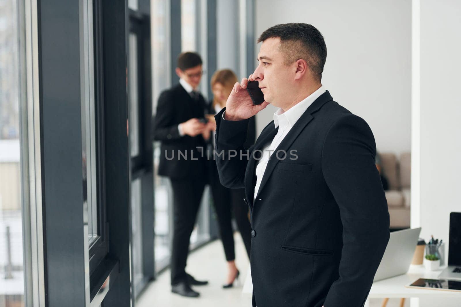 Man holds phone. Group of people in official formal clothes that is indoors in the office.
