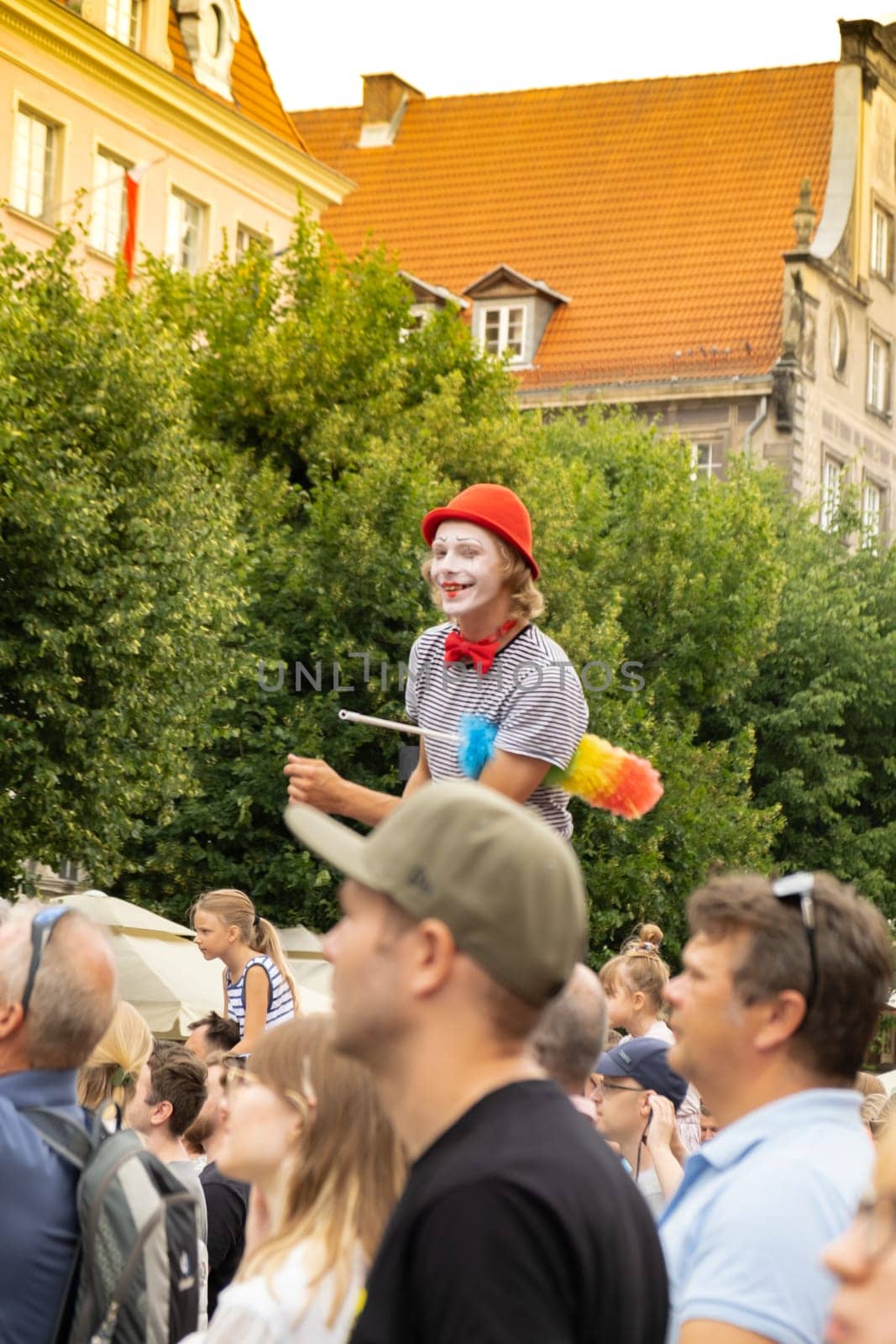 Gdansk, Poland - 9 August 2022 Portrait of cool clown in bright wig. Parade during Dominic's Fair in Gdansk. Entertainment festival in street stilts walker man in red juggling smiling by anna_stasiia