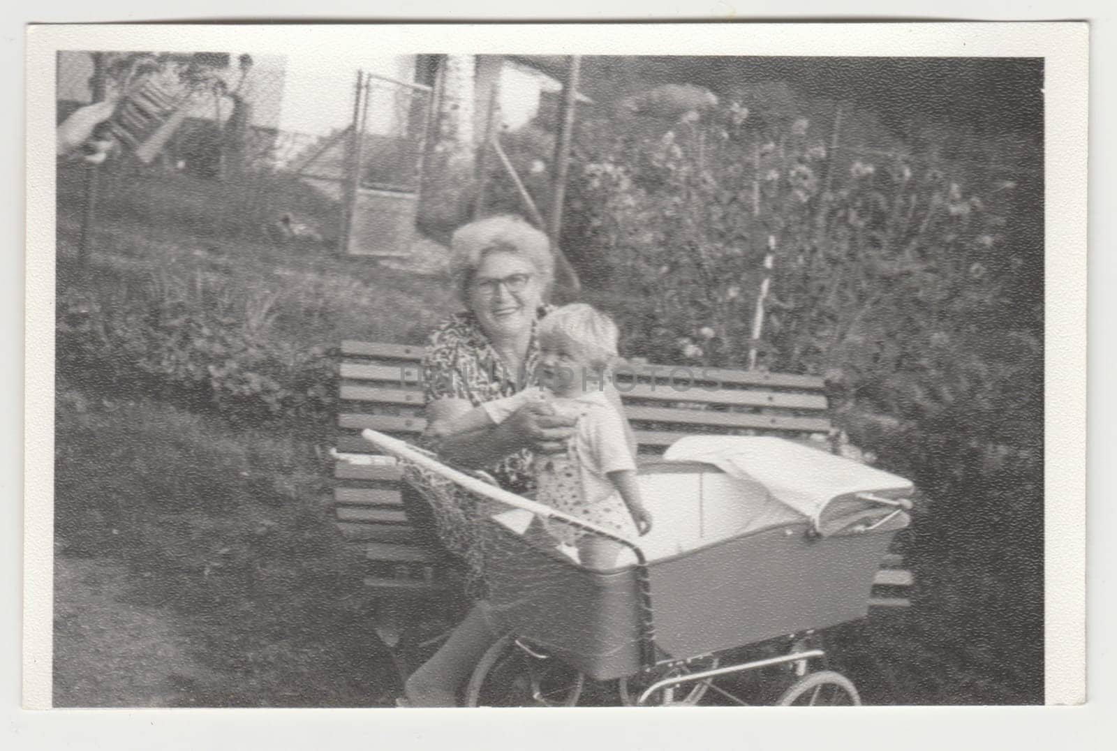 Vintage photo shows grandmother holds a toddler in the pram - carriage. Retro black and white photography. Circa 1980s. by roman_nerud