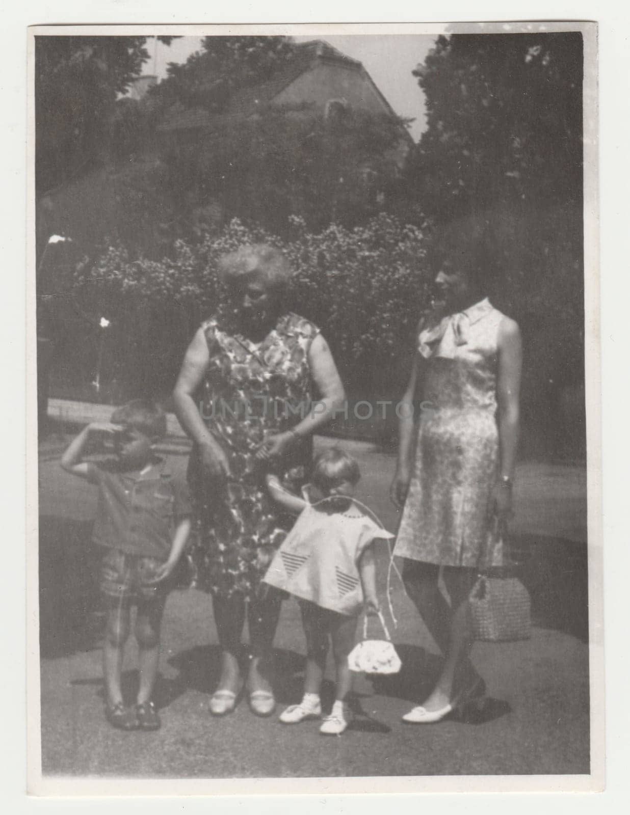 Vintage photo shows mother and grandmother with children outdoors. Retro black and white photography. Circa 1970s. by roman_nerud