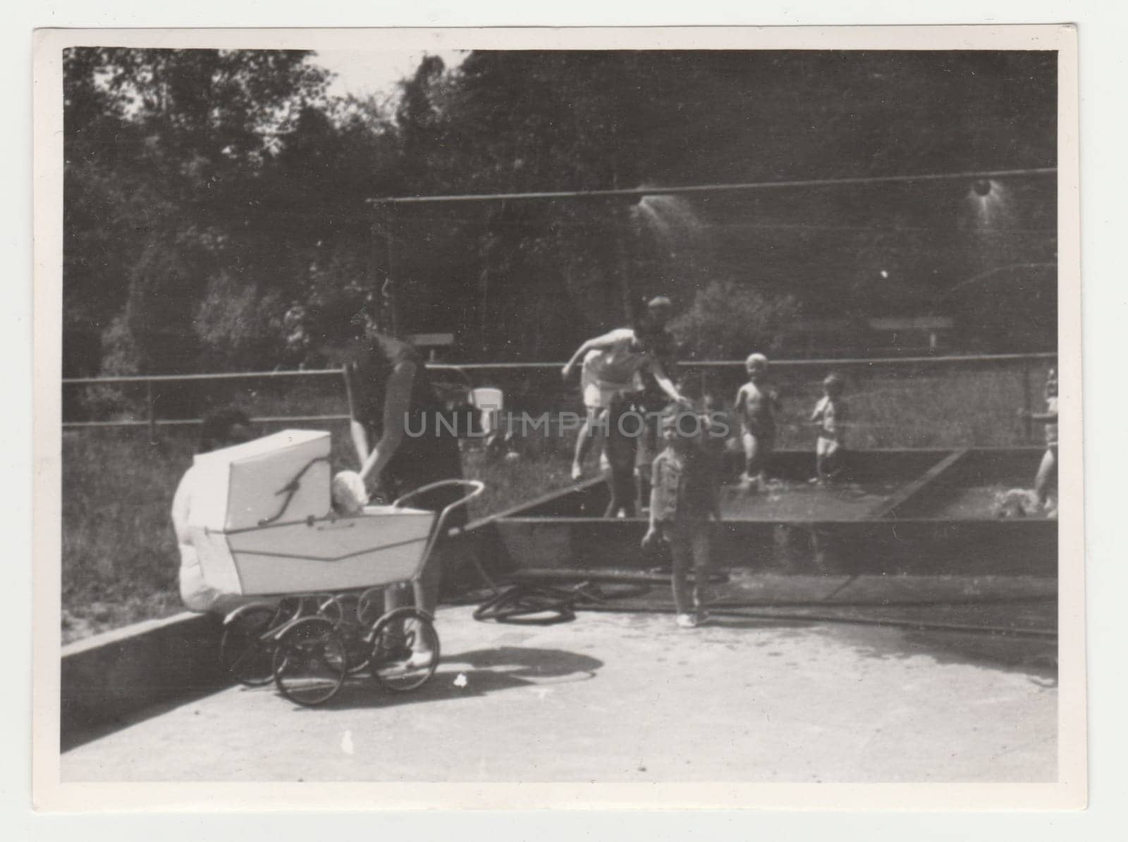 Vintage photo shows mothers with children at the playground - outdoor showers. Retro black and white photography. Circa 1970s. by roman_nerud