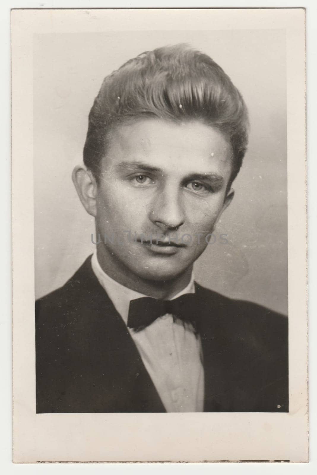 Vintage photo shows a young man. He wears black jacket and bow tie. Studio portrait. Retro black and white photography. Circa 1960s. by roman_nerud