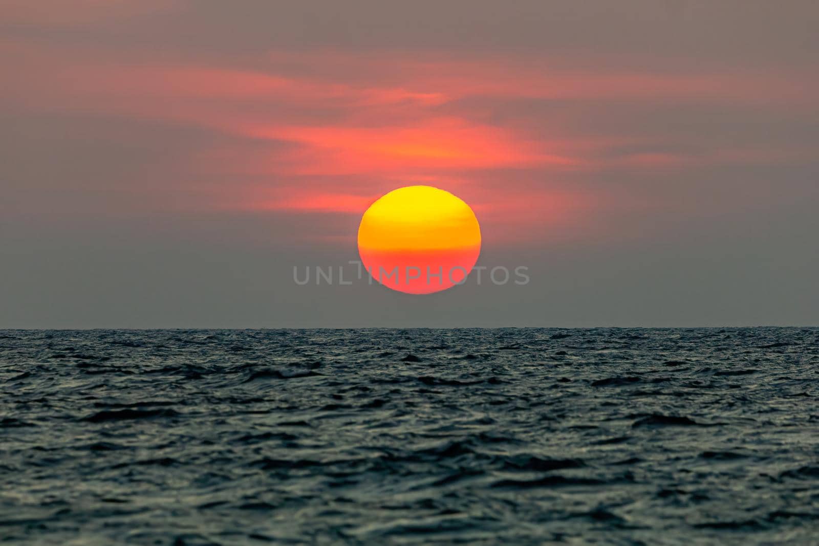 The sun is falling into the sea. , The sky is orange And the sea is dark
