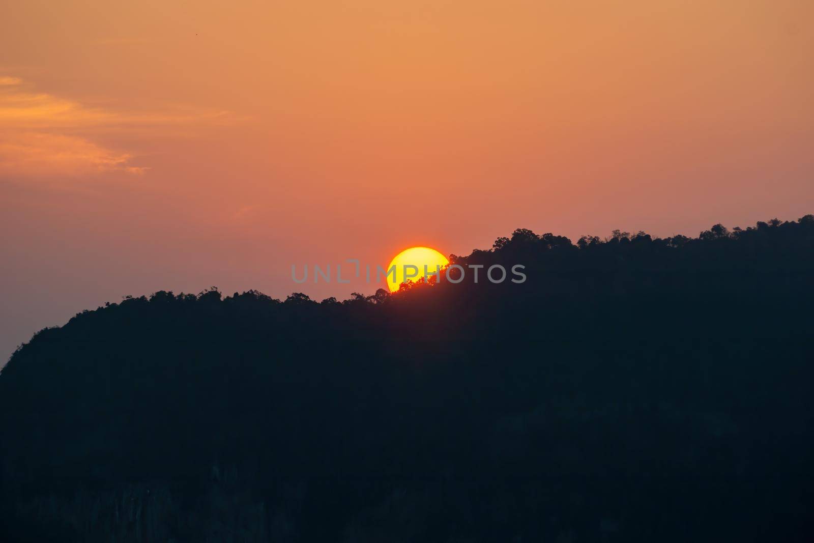 Sunrise behind the mountains, the shadows of the mountains, the orange sky with faint clouds.