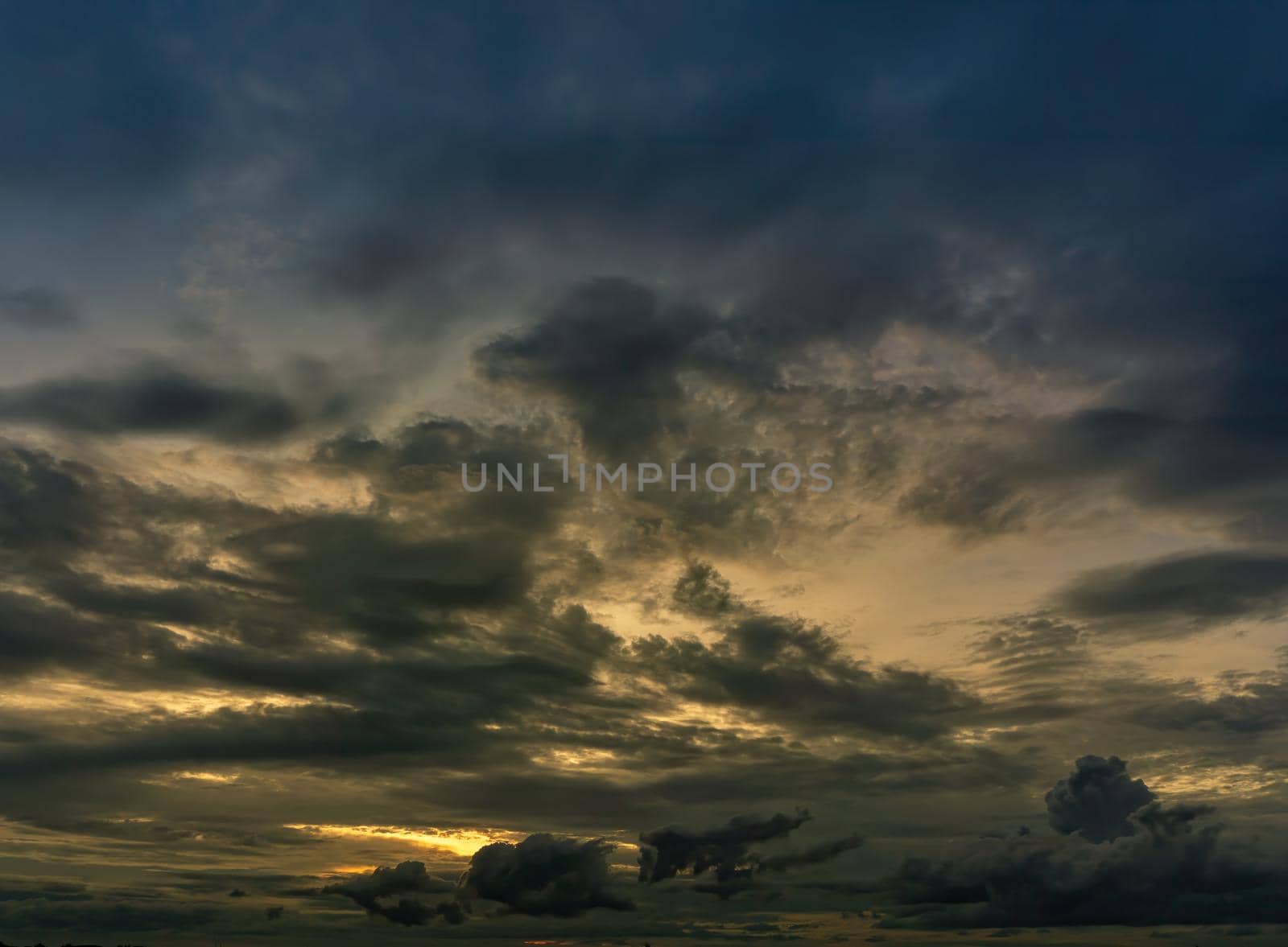 The clouds filled the sky, obscuring the light from the sun during the sunset. The sky in the middle is coloured orange from the sun. The bottom and top sky are black and dark blue from the rain clouds.