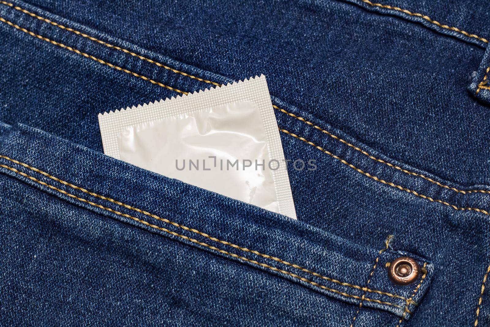 Condom in white packaging in jeans pocket close up