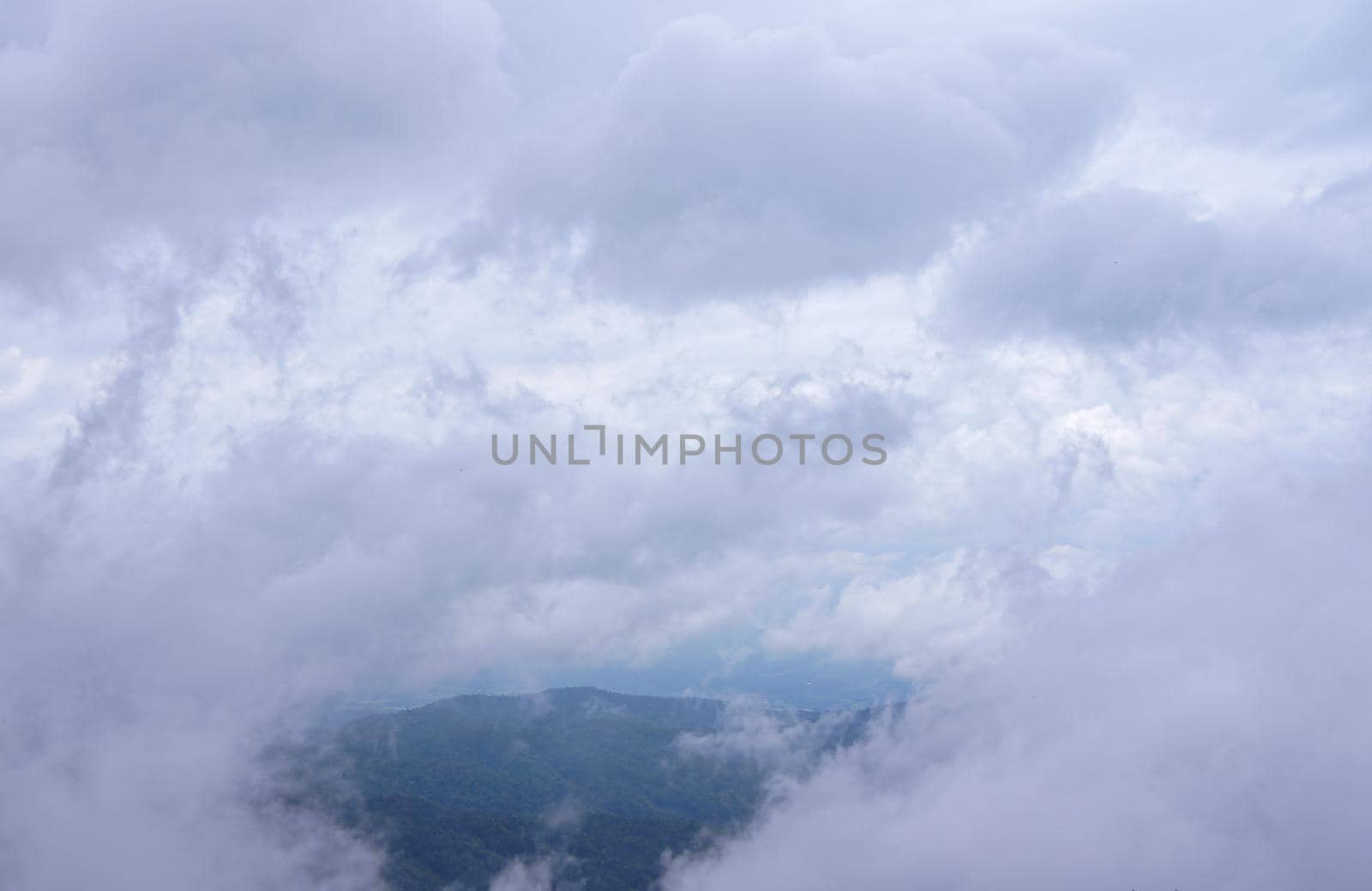 Clouds and fog are soft fluffy scattered all over, passing through gaps, seeing as green mountains.