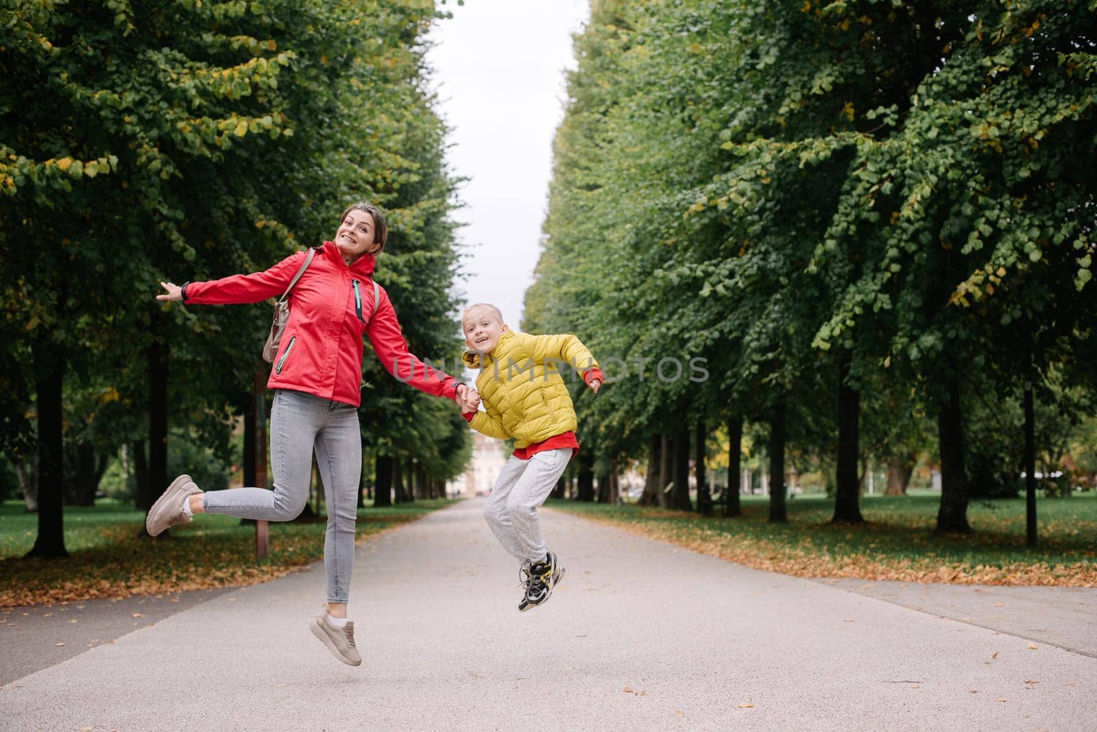 Mother and son jumping in the autumn park. Fall Season. Happy young beautiful mother and her son have a walk in the park by Andrii_Ko