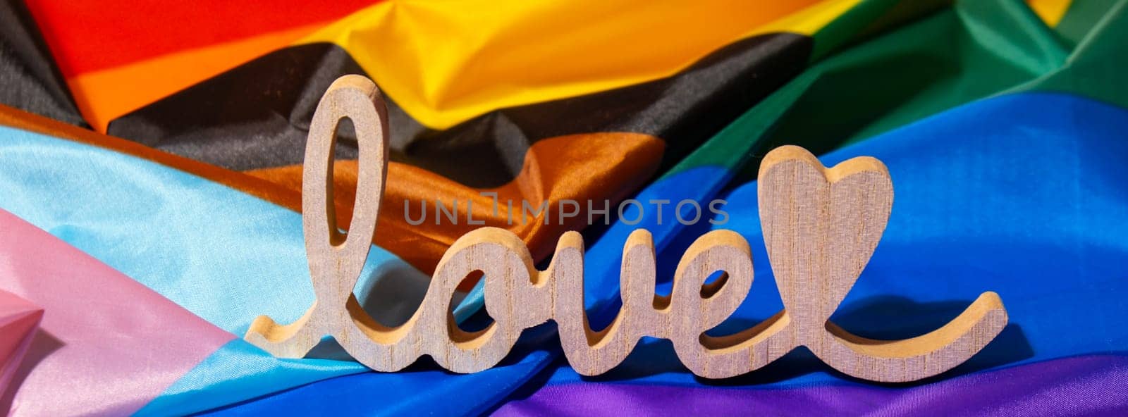 Banner Wooden word love with heart romance on Rainbow LGBTQIA flag made from silk material. Valentine's Day greeting card. Symbol of LGBTQ pride month. Equal rights. Peace and freedom. Support LGBTQIA community. Diversity equality