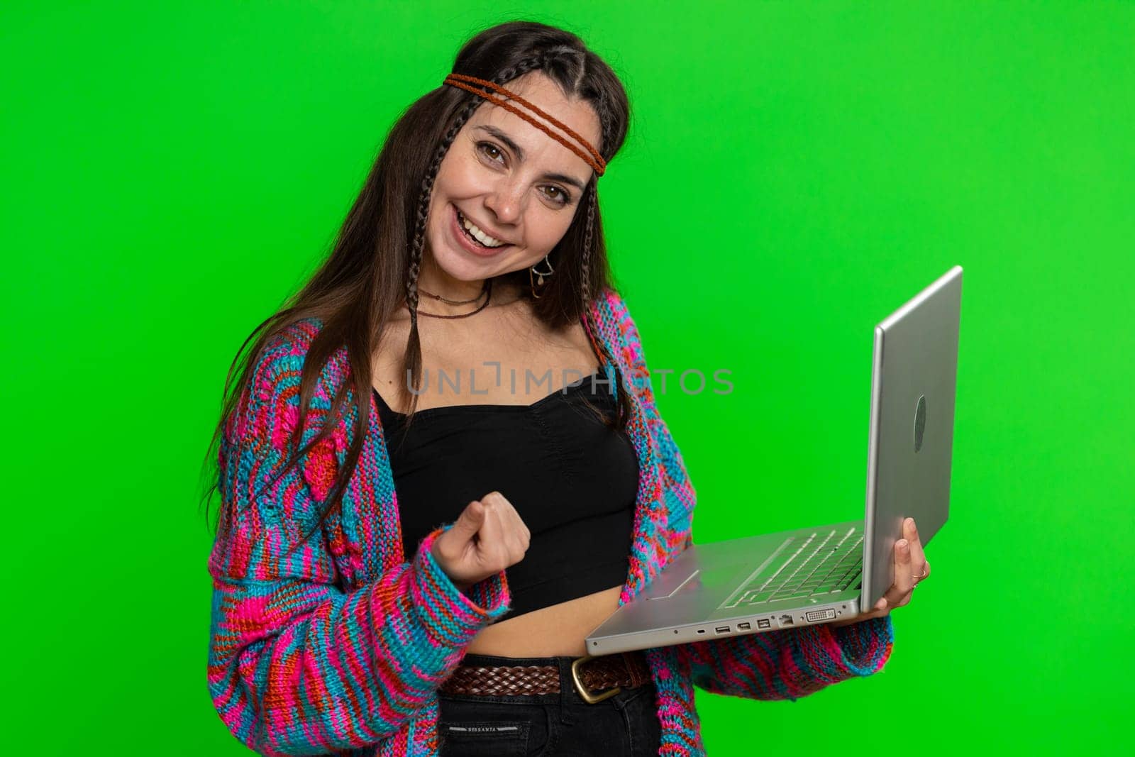 Excited happy young hippie woman typing on laptop computer, working on project, enjoying results, winning lottery, celebrating success online shopping win. Girl isolated on green chroma key background