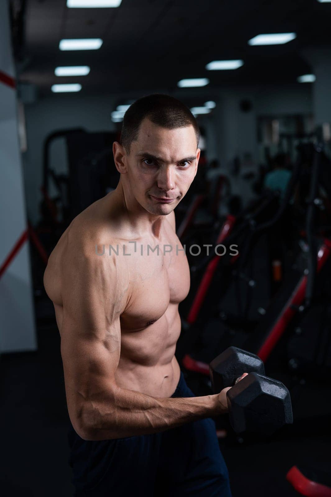 Shirtless man doing bicep exercises with dumbbells in the gym