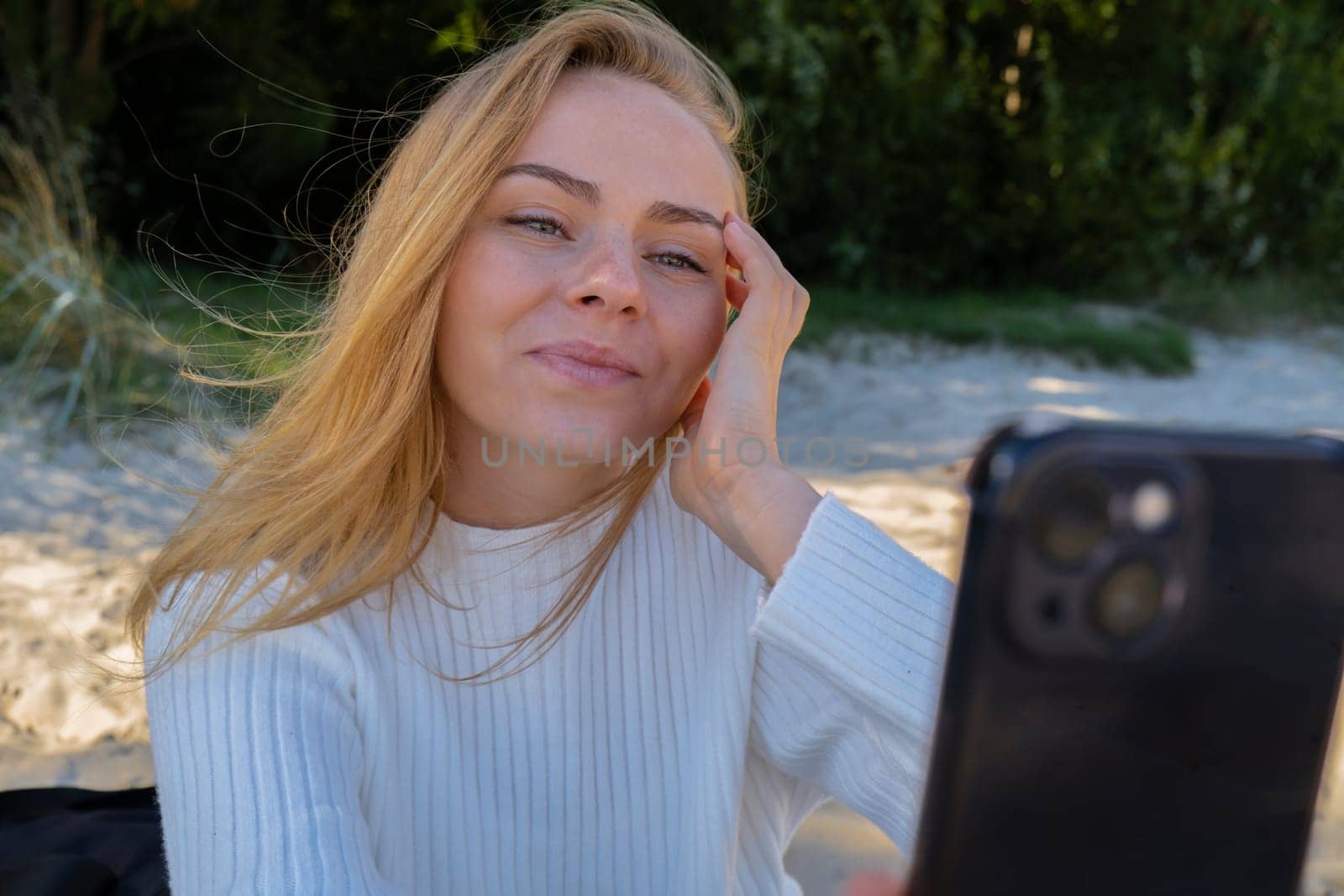 Portrait of Happy young woman take selfie on the beach sea ocean. Smiling to camera while making video call. Influencer and content creator on social media. Leisure in nature. Wellbeing unity with nature health mindfulness. Vacation and technology Enjoy outdoor lifestyle relaxation