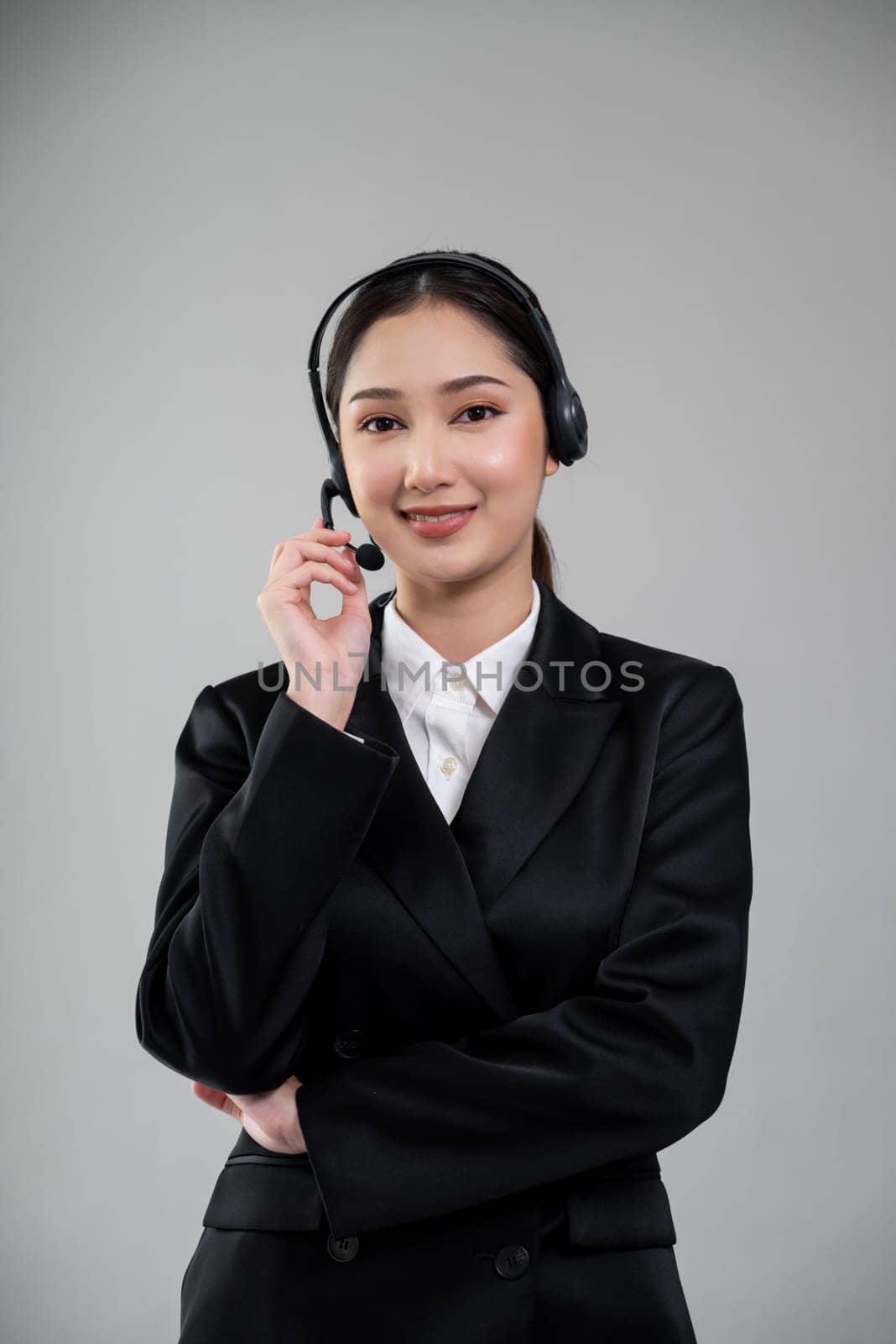 Attractive asian female call center operator with happy smile face advertises job opportunity on empty space, wearing a formal suit and headset on customizable isolated background. Enthusiastic