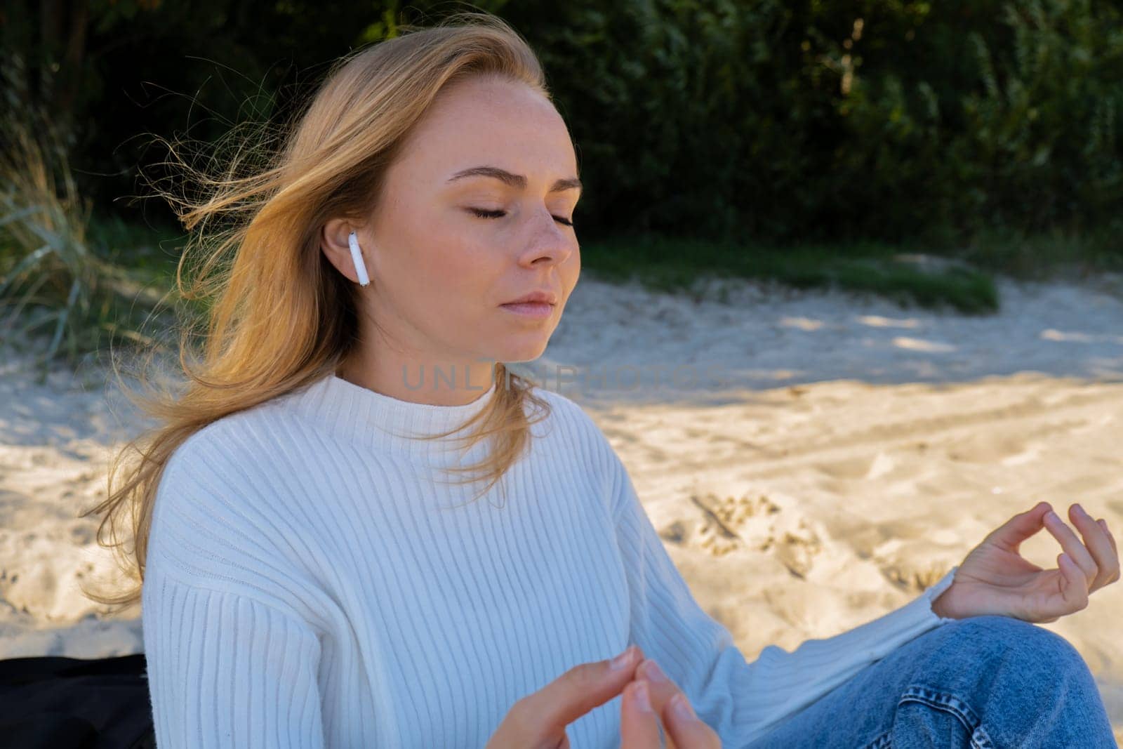 Happy young woman on the beach sea ocean. Wearing wireless headphones doing audio healing sound therapy being mindful Leisure in nature. Wellbeing unity with nature health mindfulness. Enjoy outdoor lifestyle relaxation