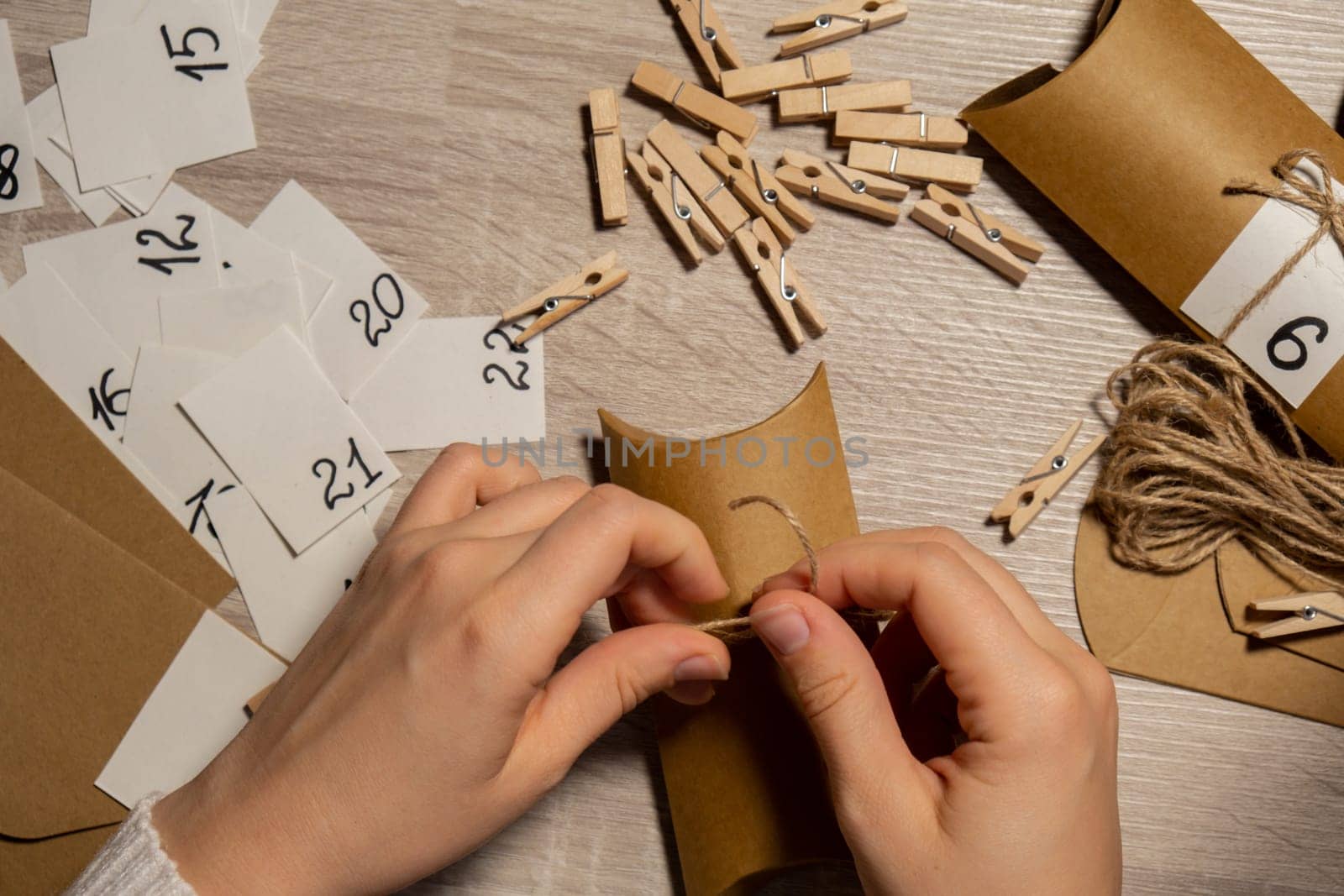 Unrecognizable young woman sticks number on craft bag, fastens with clothespin. Female making kraft paper for homemade advent calendar Made with your own hands step by step DIY crafts do it yourself. Preparation to christmas concept. Seasonal activities for children family winter holidays. Eco friendly presents gifts. open the package every day