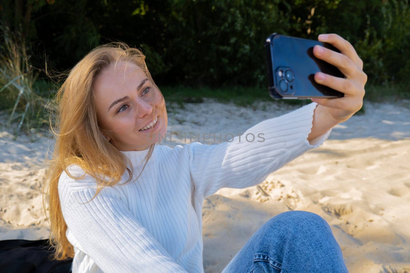 Portrait of Happy young woman take selfie on the beach sea ocean. Smiling to camera while making video call. Influencer and content creator on social media. Leisure in nature. Wellbeing unity with nature health mindfulness. Vacation and technology Enjoy outdoor lifestyle relaxation