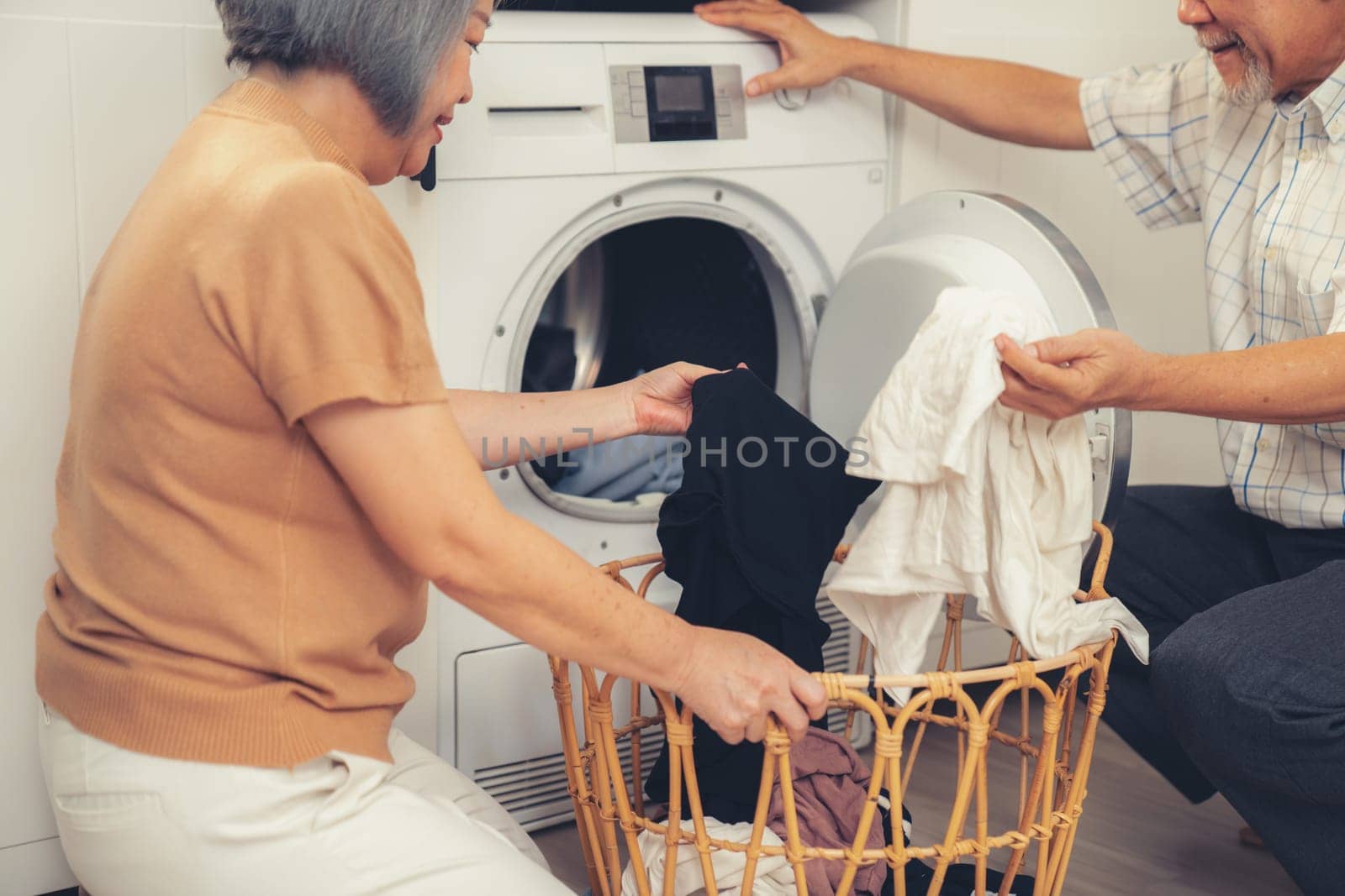 Senior couple working together to complete their household chores at the washing machine in a happy and contented manner. Husband and wife doing the usual tasks in the house.