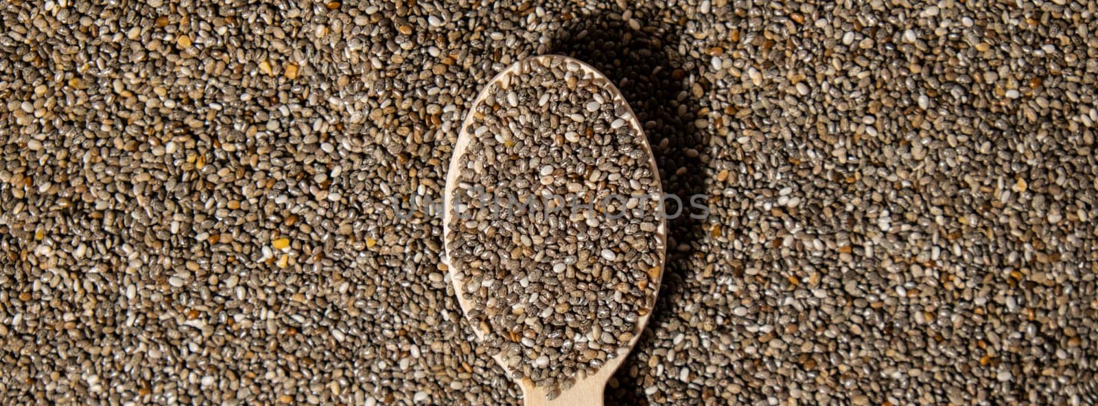 Chia seeds in wooden spoon. Healthy superfood rich in Omega 3 fatty acids. Dry healthy natural ingredient. Chia grains are falling. Vegetarian food