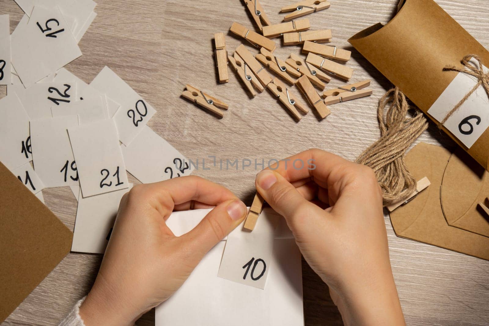 Unrecognizable young woman sticks number on craft bag, fastens with clothespin. Female making kraft paper for homemade advent calendar Made with your own hands step by step DIY crafts do it yourself. Preparation to christmas concept. Seasonal activities for children family winter holidays. Eco friendly presents gifts. open the package every day