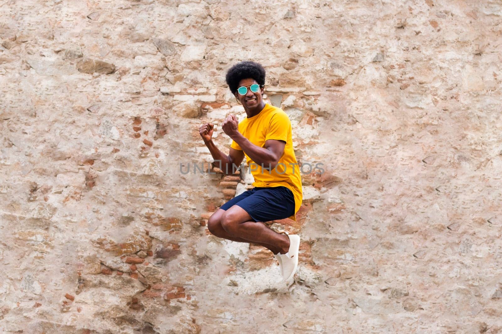 Happy young black man jumping in the air. Rustic brick and stone wall background. Happiness concept.