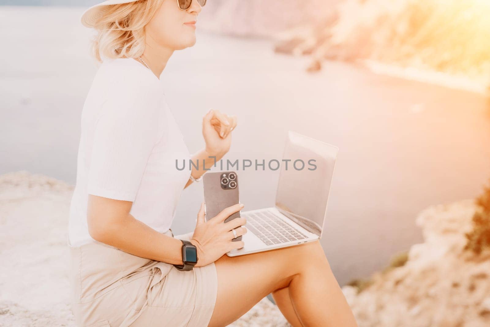 Digital nomad, Business woman working on laptop by the sea. Pretty lady typing on computer by the sea at sunset, makes a business transaction online from a distance. Freelance remote work on vacation