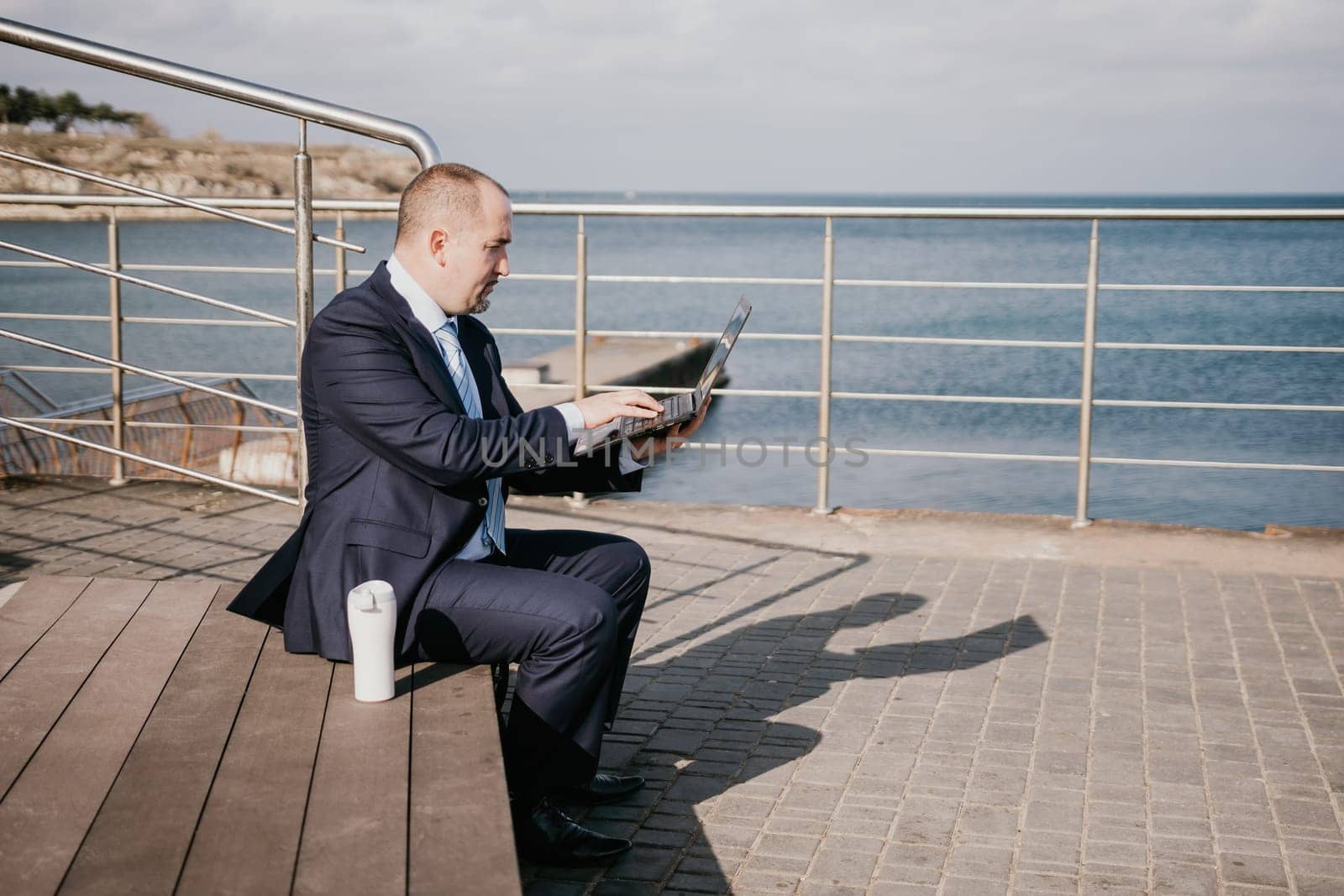 Digital Nomad, a young tattooed man working remotely online, typing on a laptop keyboard while sitting on a beach at sunset. Working remotely on vacation, running an online business from a distance